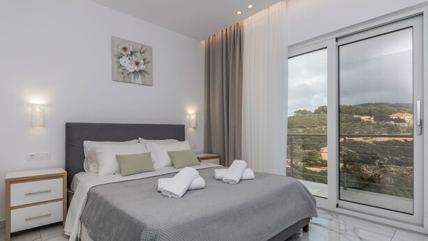 Camera da letto moderna con un letto grande, un comodino, una lampada a parete e vista sull'esterno tramite una porta scorrevole in vetro.