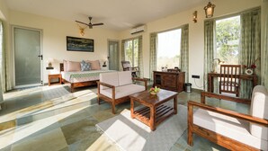 A spacious living room with a sofa, coffee table, and chairs. There is a bed with a view of the outdoors. - The Rann Baagh Ranthambore (Sawai Madhopur)