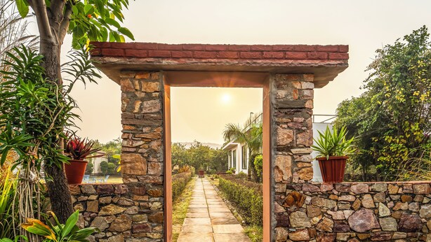 A stone pathway leading through a rustic archway surrounded by lush greenery and potted plants. - The Rann Baagh Ranthambore (Sawai Madhopur)