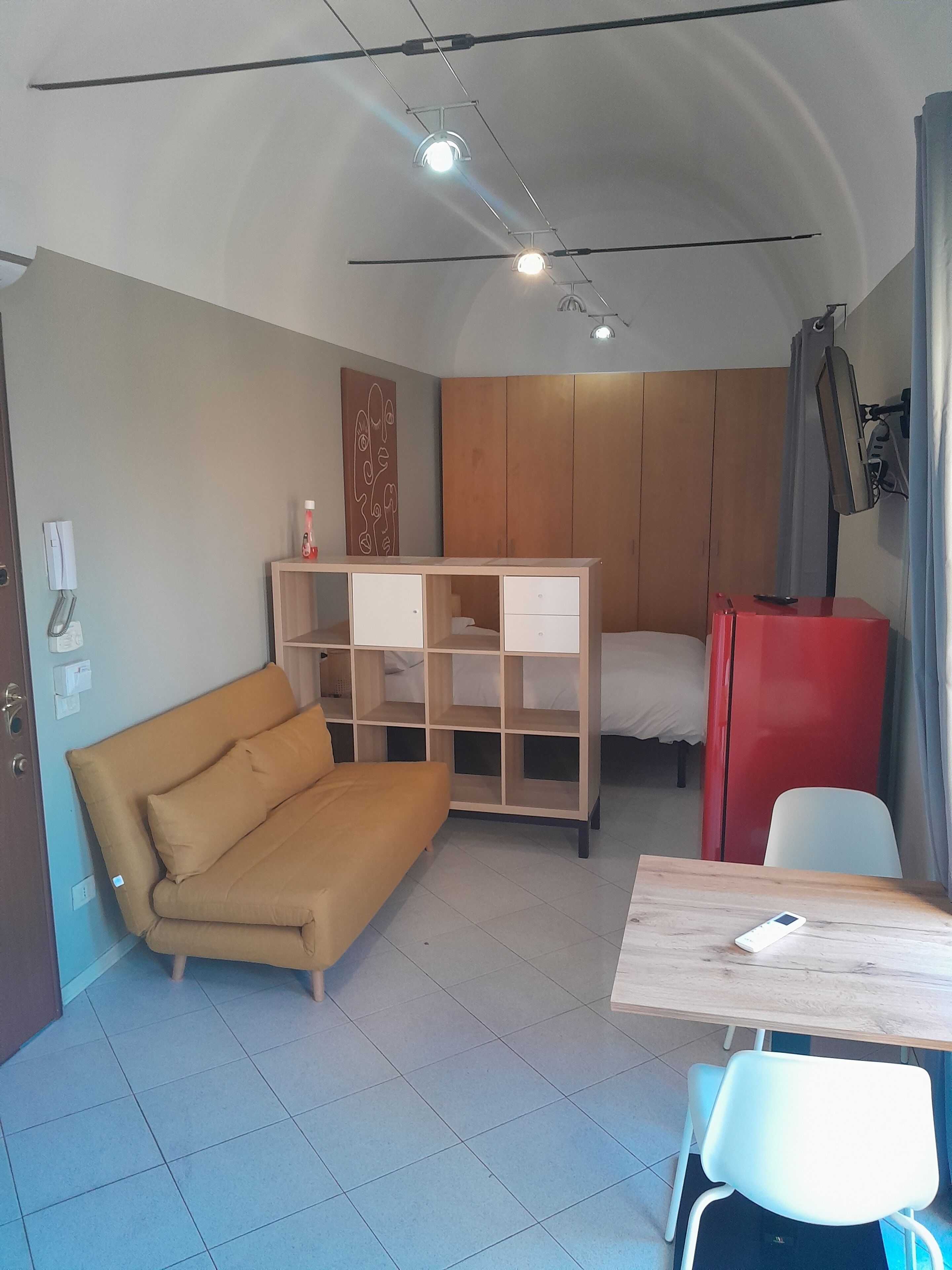 Een kleine kamer met een slaapbank, een tafeltje, een kast en een bed.