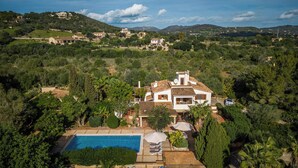 Una villa con piscina, rodeada de abundante vegetación y colinas al fondo.