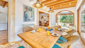 Un comedor con una mesa de madera, sillas de mimbre y vistas al exterior.