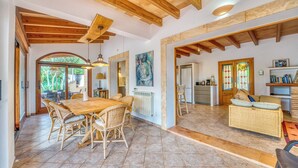 Un amplio espacio de estar con una mesa y sillas de madera para comer, una cocina al fondo y una zona de estar acogedora con un sofá y cojines.