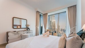 A modern hotel room with a large bed, a marble headboard, a vanity with a mirror, and a view of a cityscape through floor-to-ceiling windows. - High Floor with Direct Burj Khalifa and Fountain Views (Dubai)