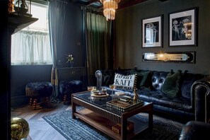 A dark-themed living room with a leather sofa, a glass coffee table, and a chandelier. - 3-Bed Historic Knitters House in Nottingham (Nottingham)