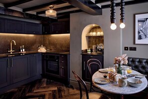 A modern kitchen with dark cabinetry, a herringbone floor pattern, and a dining area with a round table set for breakfast. - 3-Bed Historic Knitters House in Nottingham (Nottingham)