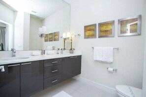 A modern bathroom with a large mirror, dark cabinets, a white sink, and artwork on the wall. - Serenity Resort 3 Bedroom Vacation Home 17419 (Clermont)