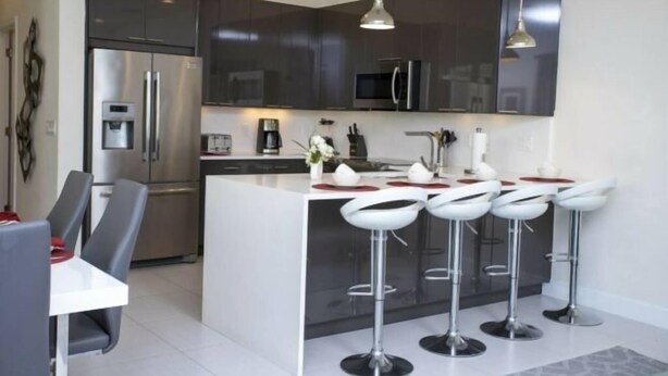 A modern kitchen with a central island, bar stools, stainless steel appliances, and pendant lighting.