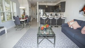 A modern living room with a glass coffee table, a sofa, and a dining area with chairs and a table.