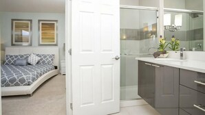 A bedroom with a bed, a bathroom with a shower, and a white door.