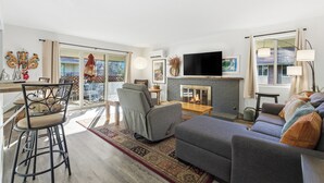 A modern living room with a fireplace, a flat-screen TV, and a dining area with a bar stool and table.