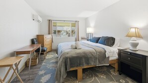 A bedroom with a bed, a desk, a chair, a nightstand, and a window with curtains.