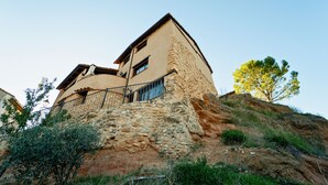 A stone building with a balcony and a tree on a hill.