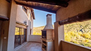 A covered patio with a brick oven, a sliding glass door leading to an outdoor dining area, and a view of a hilly landscape.