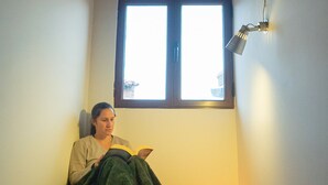 A room with a wooden ceiling, a window with a view, a reading lamp, and a candle on the floor.