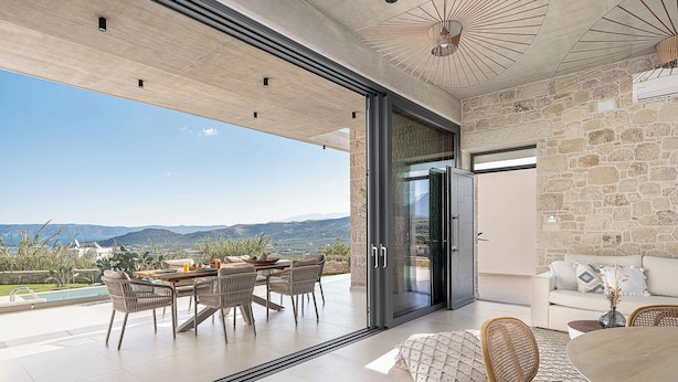 A modern open-plan living area with a dining set, a sofa, and a view of the mountains. - Himmel Villas | Seaview Luxury & 2 Private Pools (Chania)