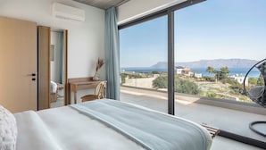 A bedroom with a large window, a bed, a desk, and a chair. - Himmel Villas | Seaview Luxury & 2 Private Pools (Chania)