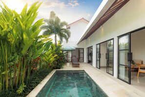 Une maison moderne avec une piscine, entourée d’une végétation luxuriante et dotée d’une terrasse avec des meubles d’extérieur.