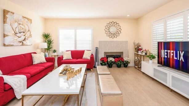 A living room with a red sofa, white coffee table, and a fireplace. There is a TV on the wall and a flower arrangement on the floor. - Beautiful Yard 7 Rooms 4 Bathrooms Near Disneyland (Hacienda Heights)