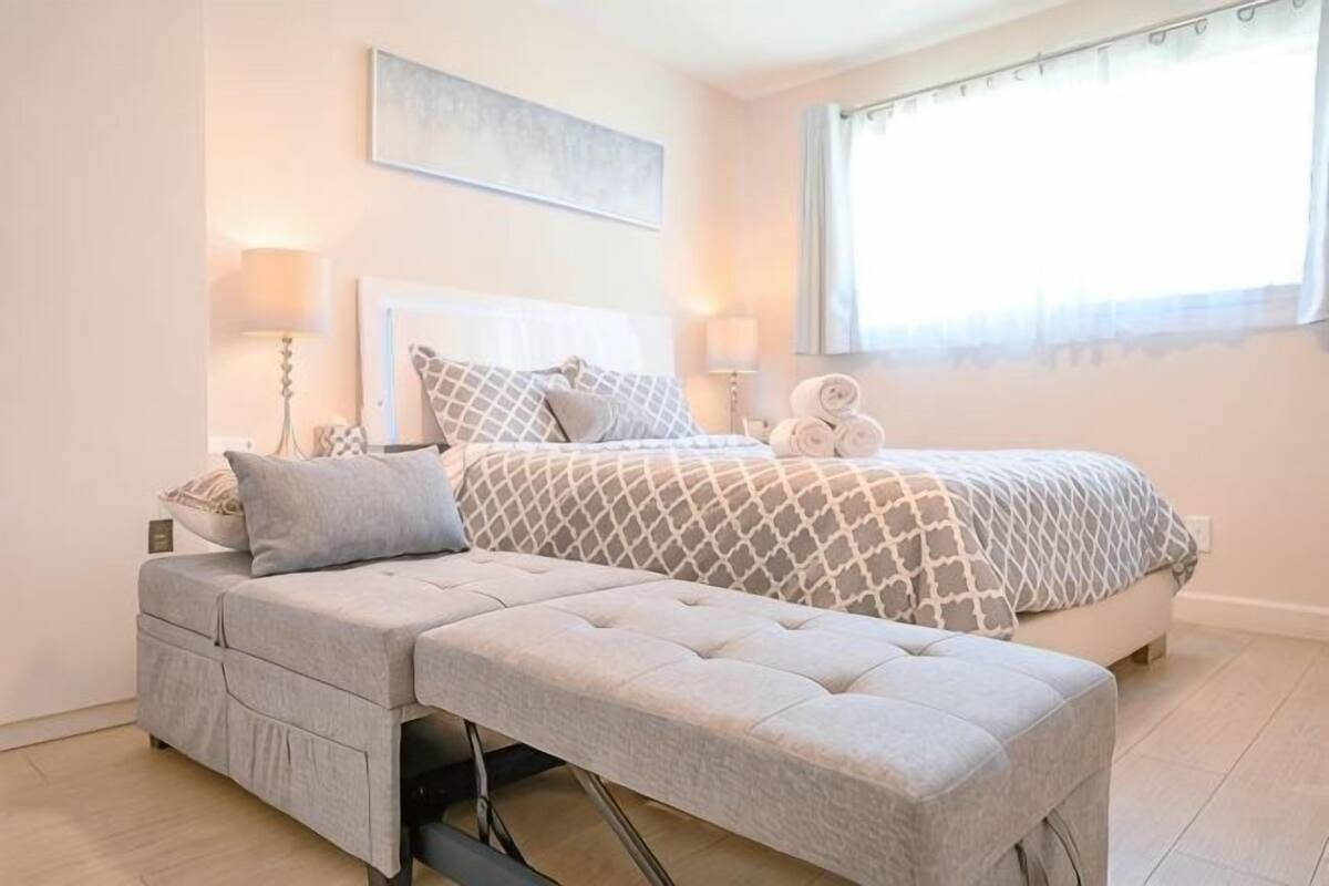 A bedroom with a bed, bedside tables, a bench, and a window.