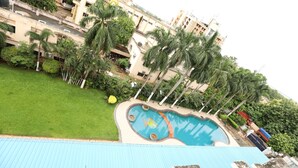A swimming pool surrounded by palm trees and a grassy area, with buildings in the background. - Hotel Prachi (Bhubaneshwar)