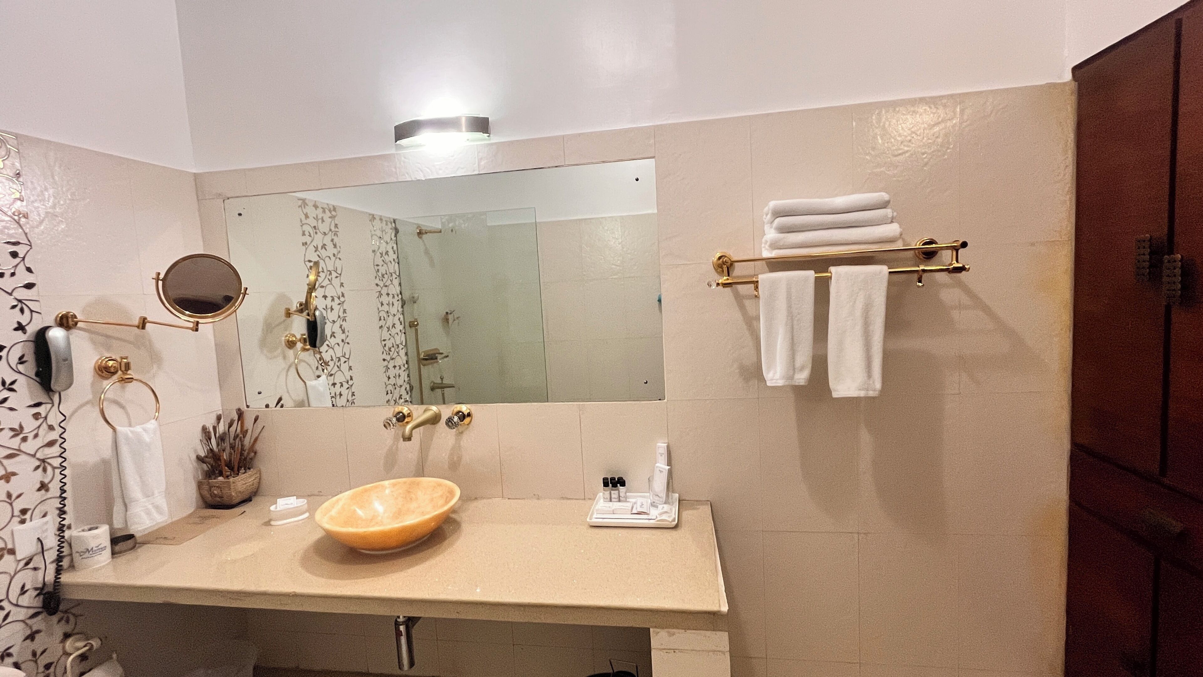 A bathroom with a beige sink, a large mirror, and a towel rack with folded towels.