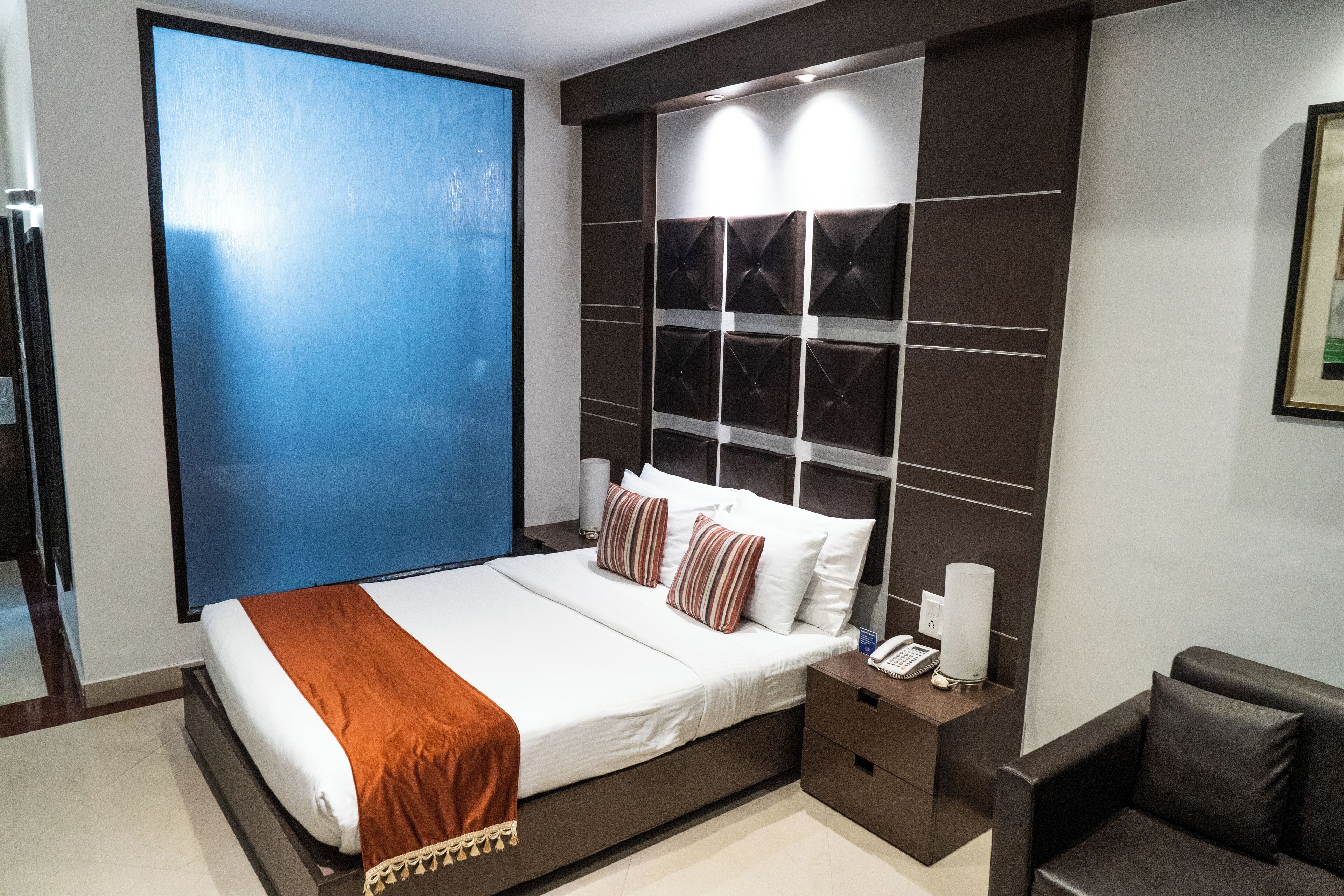 A modern hotel room with a large bed, a bedside table with a lamp, and a view of the city.
