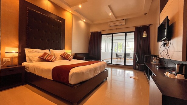 A hotel room with a large bed, a desk, a TV, and a view of the outdoors. - Hotel Prachi (Bhubaneshwar)