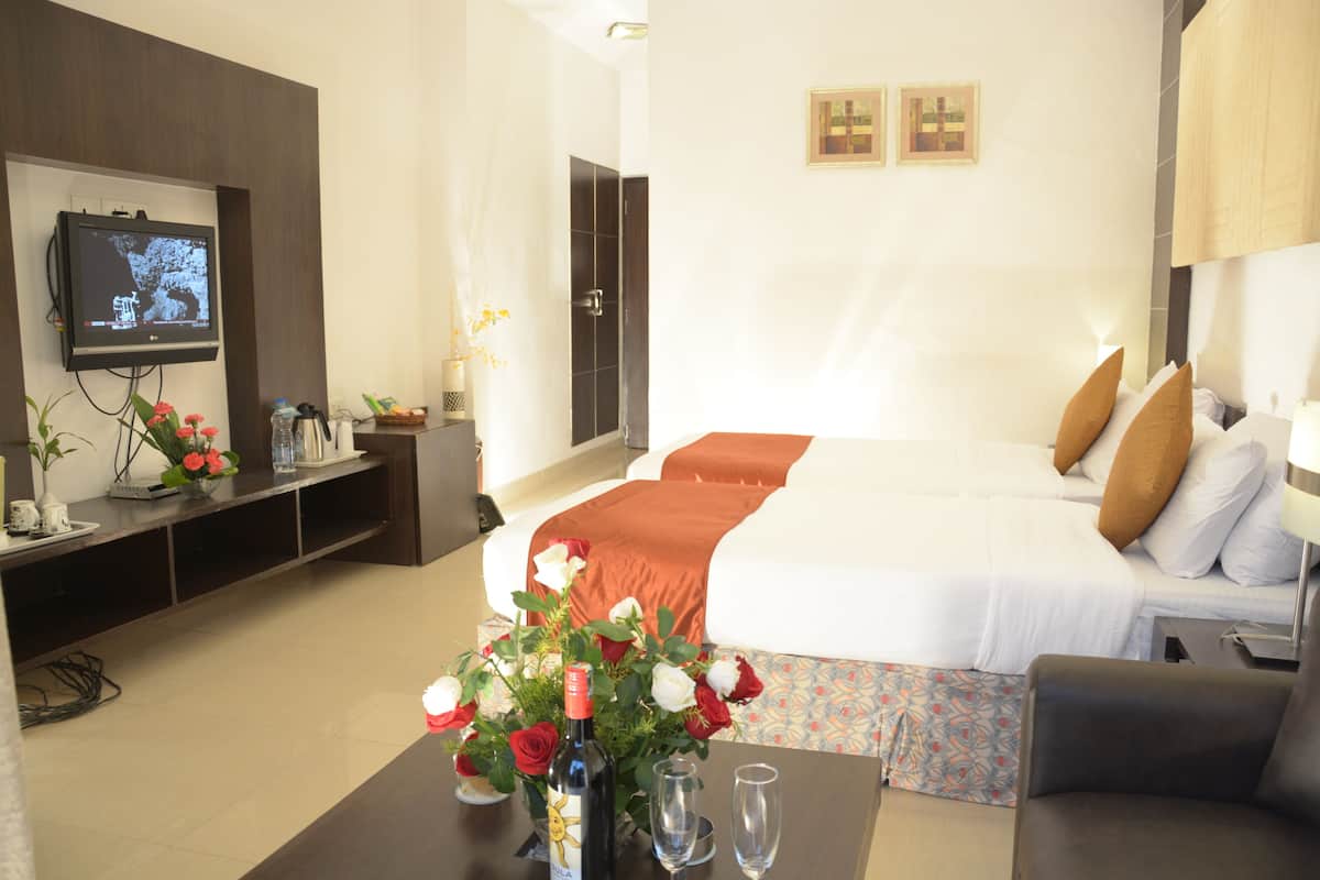 A hotel room with a bed, a TV mounted on the wall, a coffee table with flowers and glasses, and a sofa.