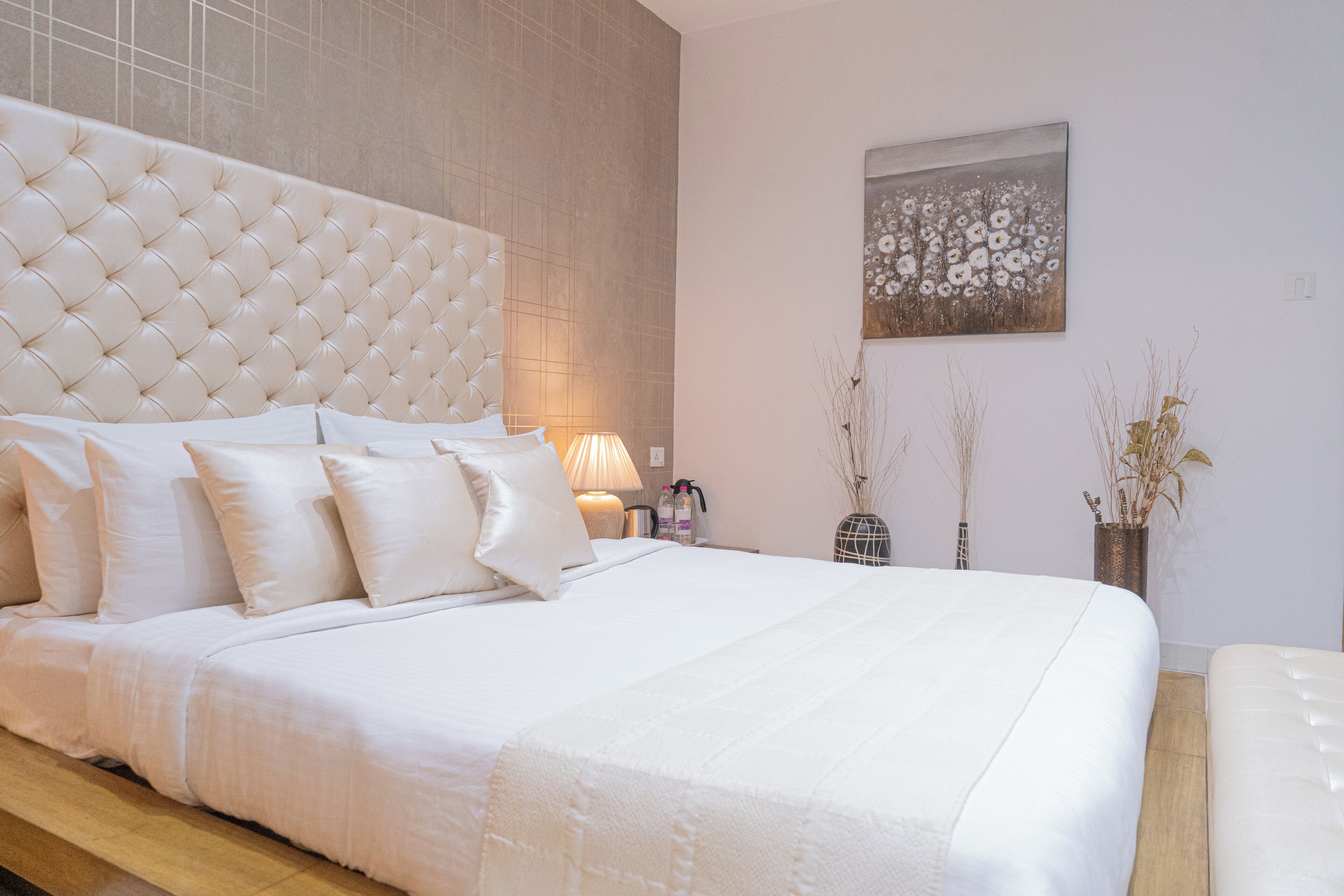 Una cama grande con cabecera capitonada, ropa de cama blanca y una mesita de noche con lámpara.