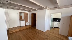 A spacious room with wooden flooring, a built-in wardrobe, and a kitchen area visible through an open door.