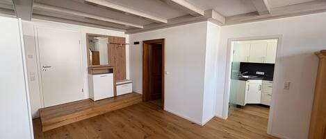 Een ruime kamer met houten vloeren, een inbouw kast en een keukenruimte zichtbaar door een open deur.