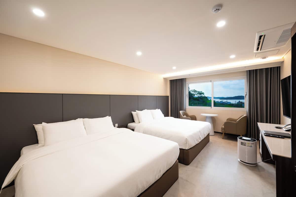 Habitación de hotel con dos camas, un escritorio, una silla, una mesita y vistas al exterior.