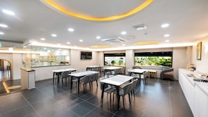 A modern restaurant with a central dining area, a bar, and a view of greenery outside. - VAVANT TOURIST HOTEL (Mokpo)