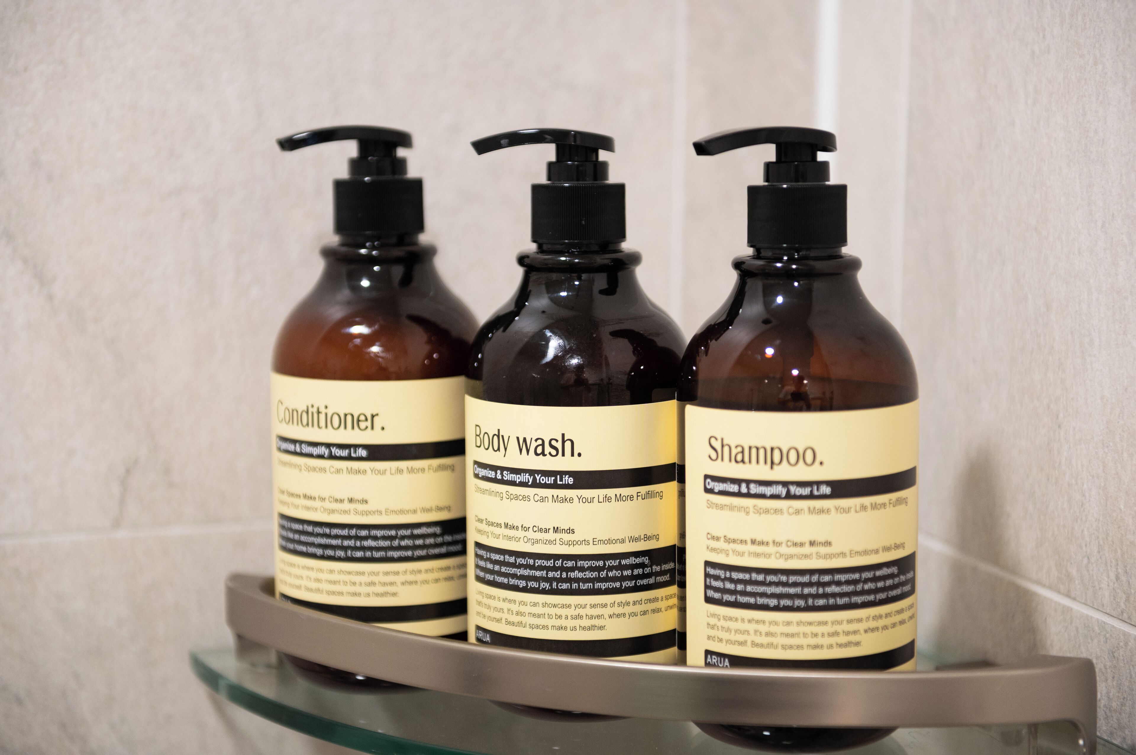 Trois bouteilles de gel douche, d’après-shampoing et de shampoing sont posées sur une étagère.