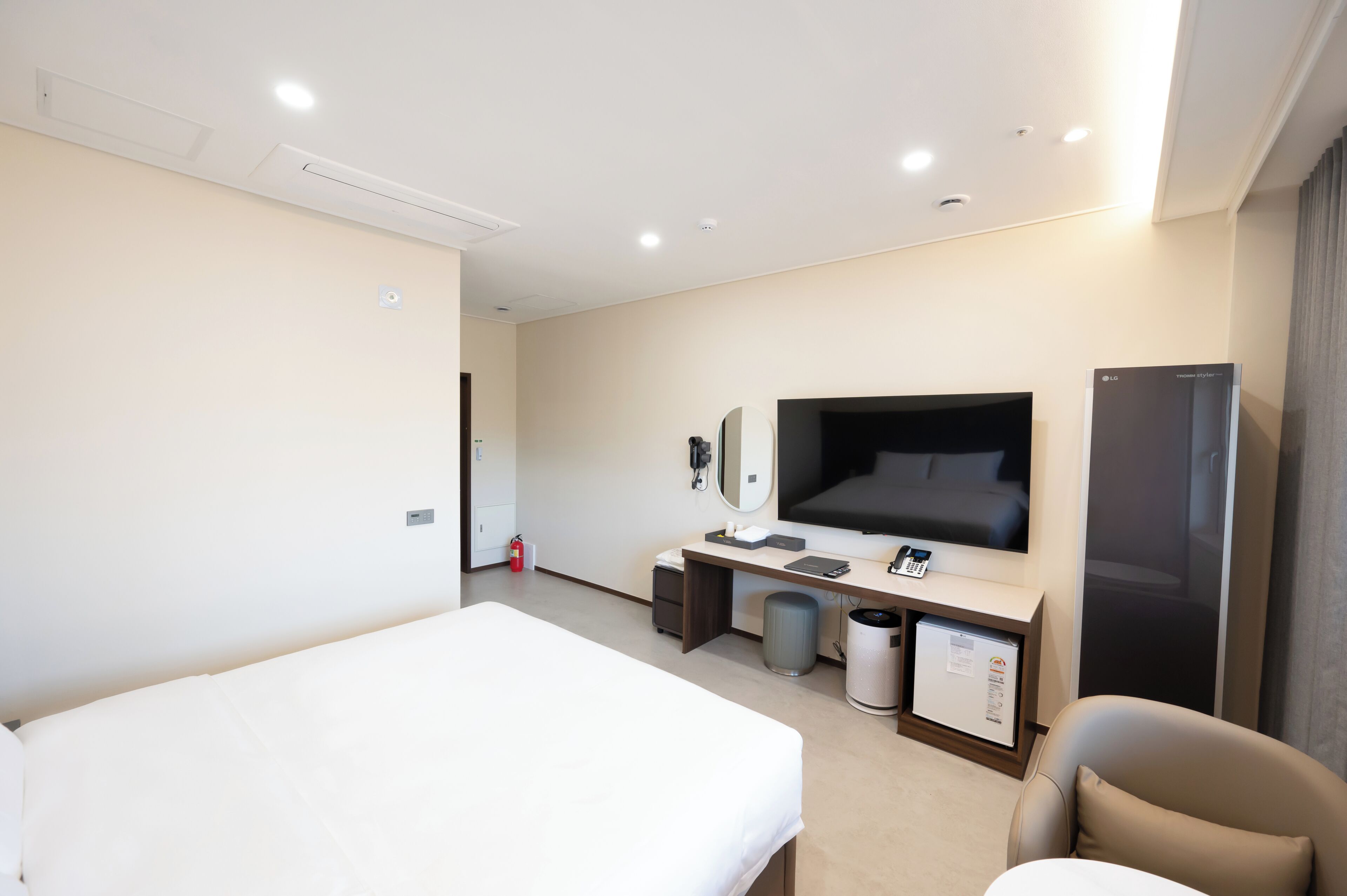 Una habitación de hotel con cama, escritorio con computadora, televisión, refrigerador y basurero.