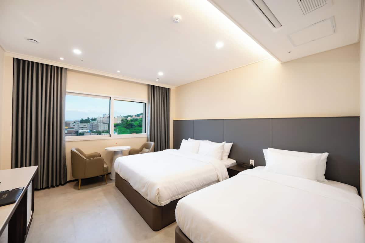 Habitación de hotel con dos camas, un escritorio, una silla y una ventana con vista a la ciudad.