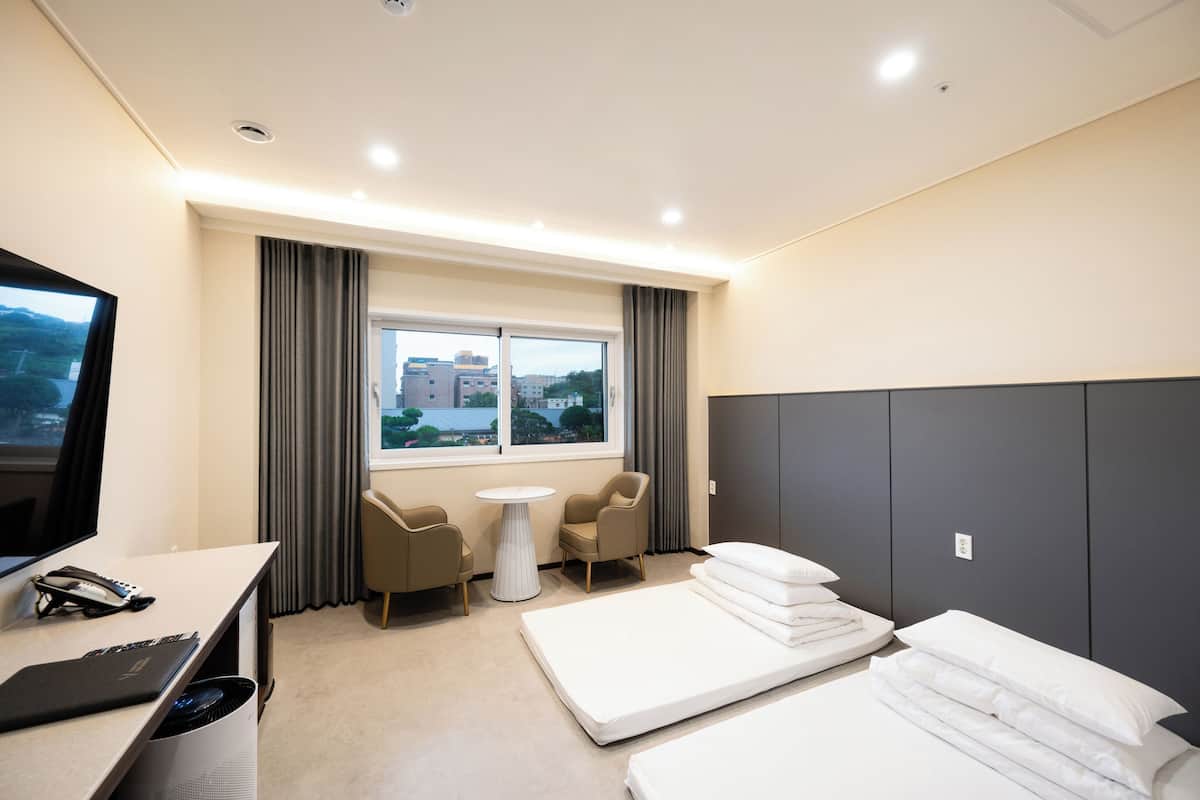 Habitación de hotel con cama, escritorio con computadora, silla, mesita y televisor.