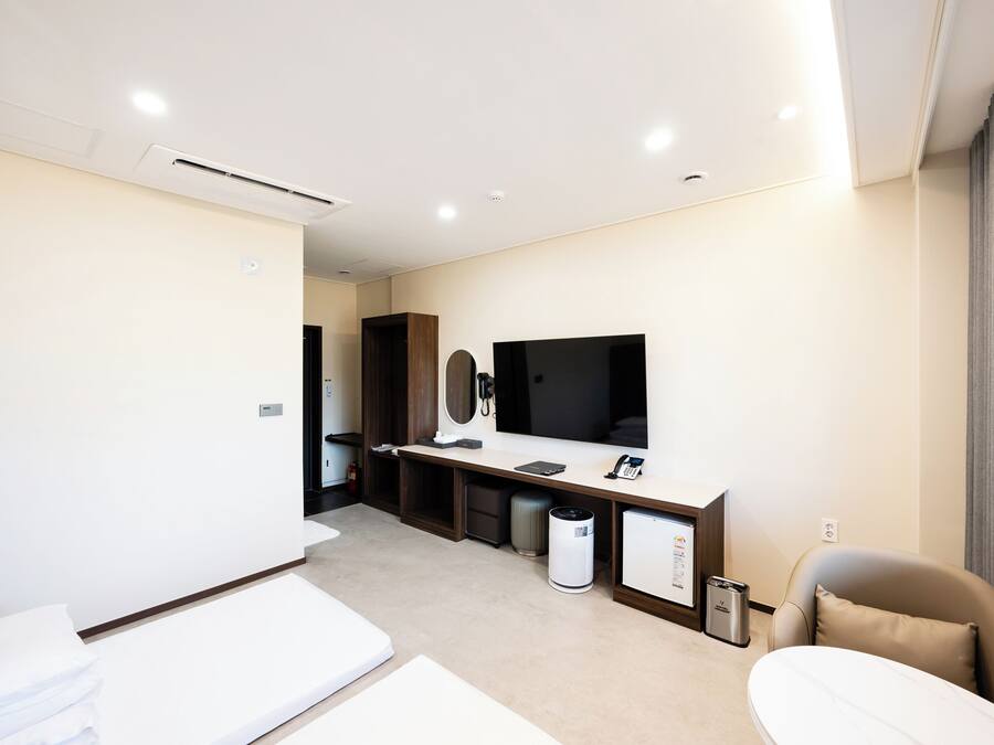 A modern hotel room with a bed, a desk with a computer, a TV, and a small kitchenette.