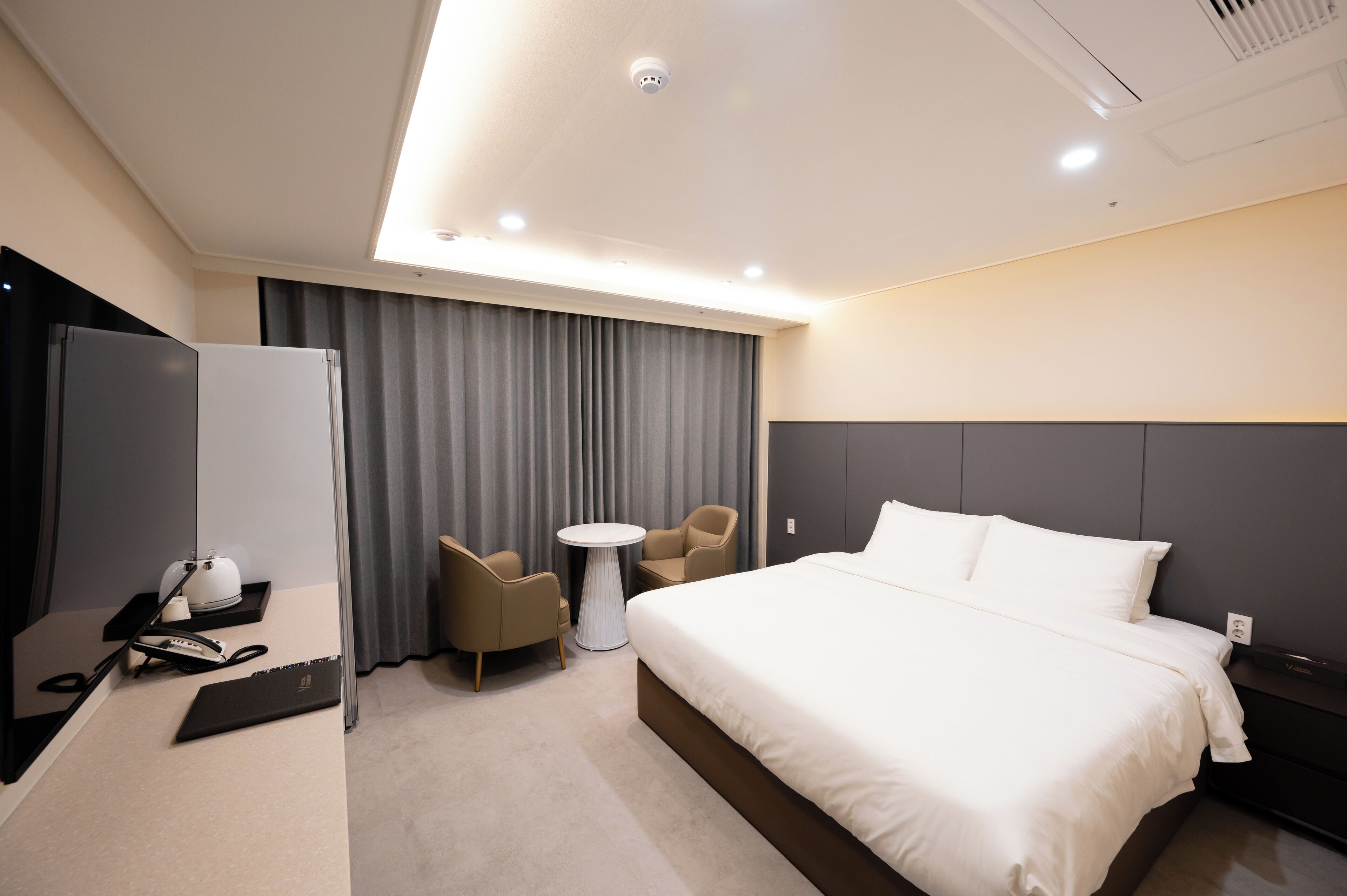 Une chambre d’hôtel moderne avec un grand lit, un bureau avec un ordinateur portable, une chaise et une petite table.