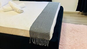 Een net opgemaakt bed met een witte dekbedsprei en een zwart-wit ruitendeken.