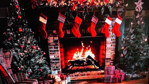 Een televisie toont een kersttafereel met een open haard, sokken en cadeaus.