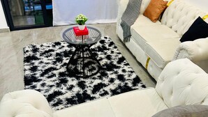 Een moderne woonkamer met een witte bank, een ronde salontafel met een rood boek en een plant, en een zwart-wit tapijt.