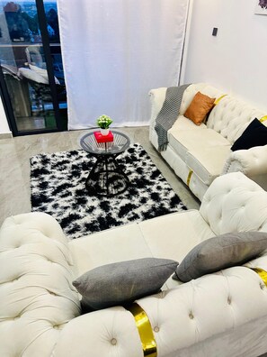 Ein modernes Wohnzimmer mit einem weißen Sofa, einem runden Couchtisch mit einem roten Buch und einer Pflanze, sowie einem schwarz-weißen Teppich.