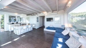 Amplia sala de estar con un sofá grande, una cocina con barra y vistas al exterior.