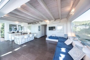 Ein großzügiger Wohnbereich mit einer großen Couch, einer Küche mit Bar und Blick ins Freie.