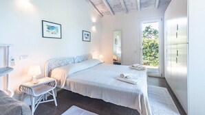 Un dormitorio con cama, mesita de noche, silla y vistas al verdor exterior.