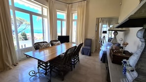 Un comedor con mesa y sillas de madera, ventanas amplias con cortinas, una chimenea de piedra y vistas al exterior.