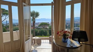 A balcony with a view of the city and mountains. There is a table with a vase of flowers and a chair. - Cannes Californie: elegant flat with sea view, parking and beach nearby. (Cannes)