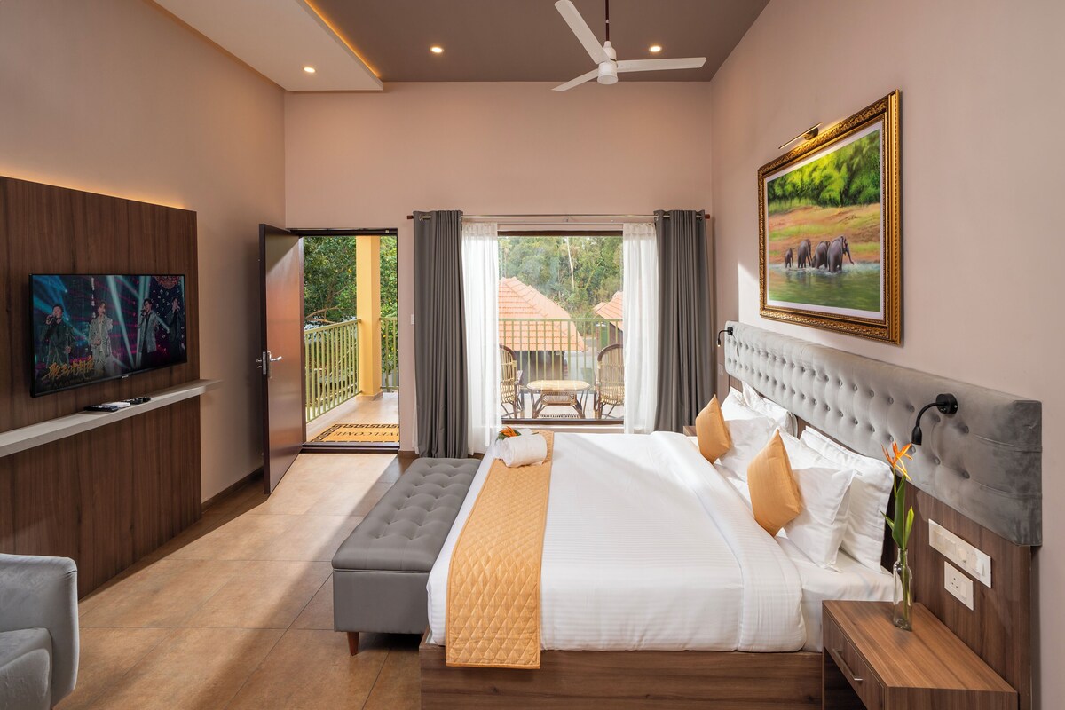 A modern hotel room with a large bed, a television, a balcony with a view of greenery, and a painting on the wall.